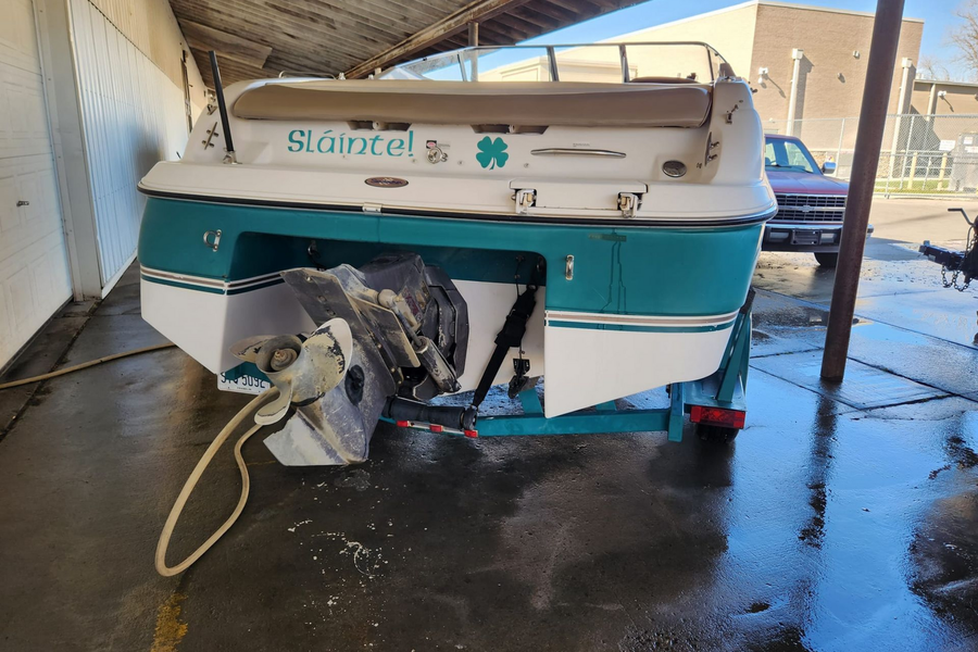 A white and teal motorboat on a trailer, parked under an open-sided shed with a concrete floor.