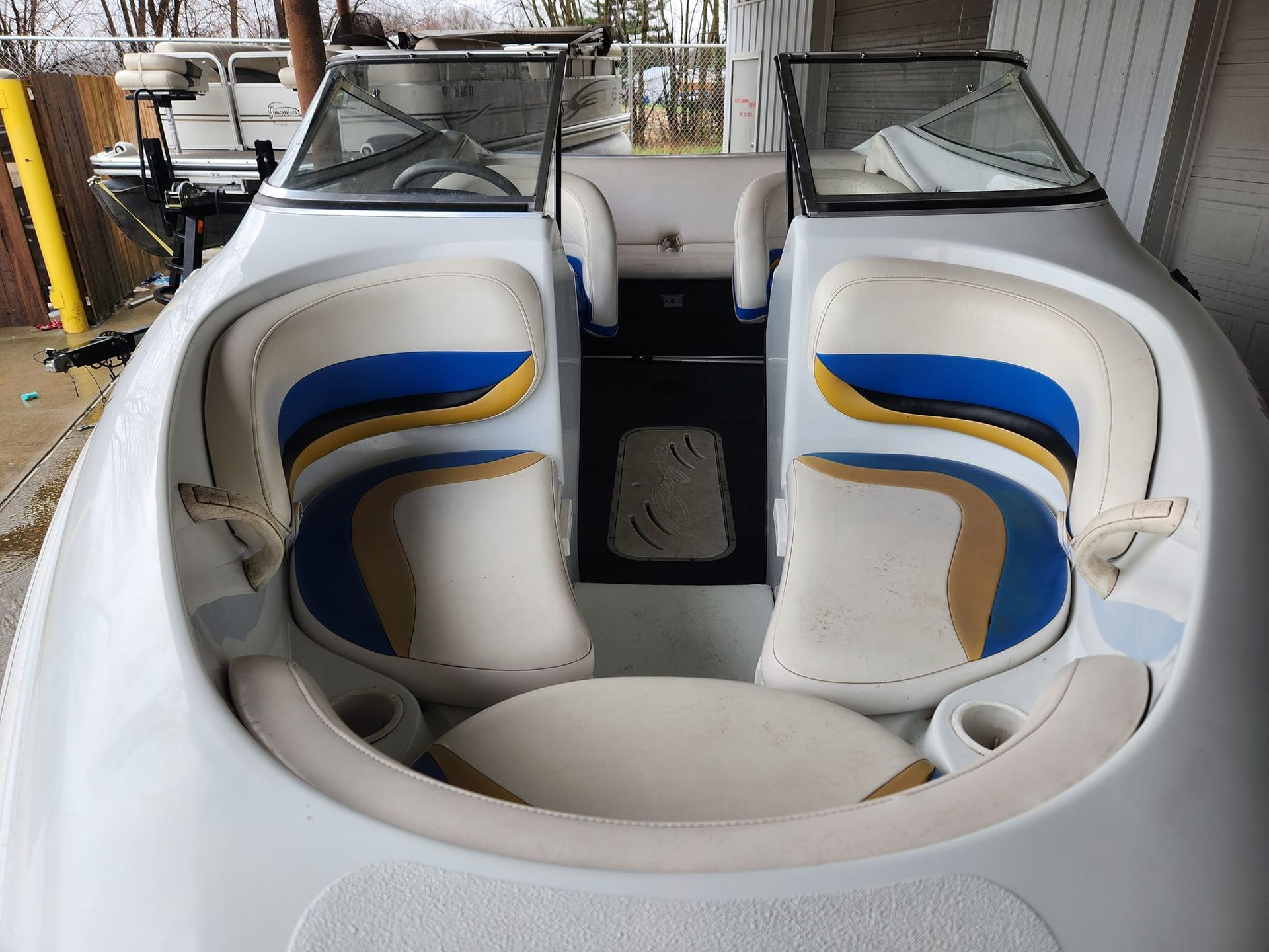 The bow seating area of a boat features white, blue, and tan vinyl upholstery and a central floor mat.