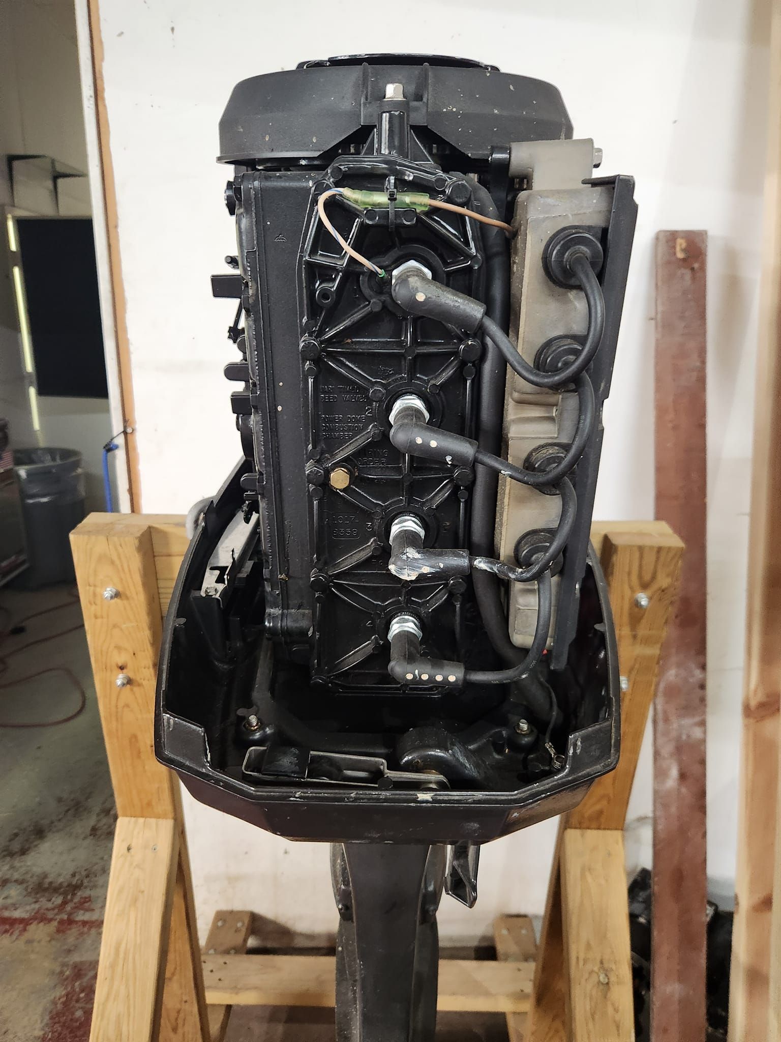 A black outboard boat motor mounted on a wooden stand, showing exposed spark plug wires and engine components.