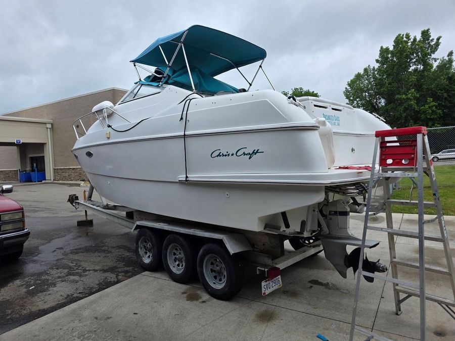 A white and teal motorboat on a trailer, parked under an open-sided shed with a concrete floor.