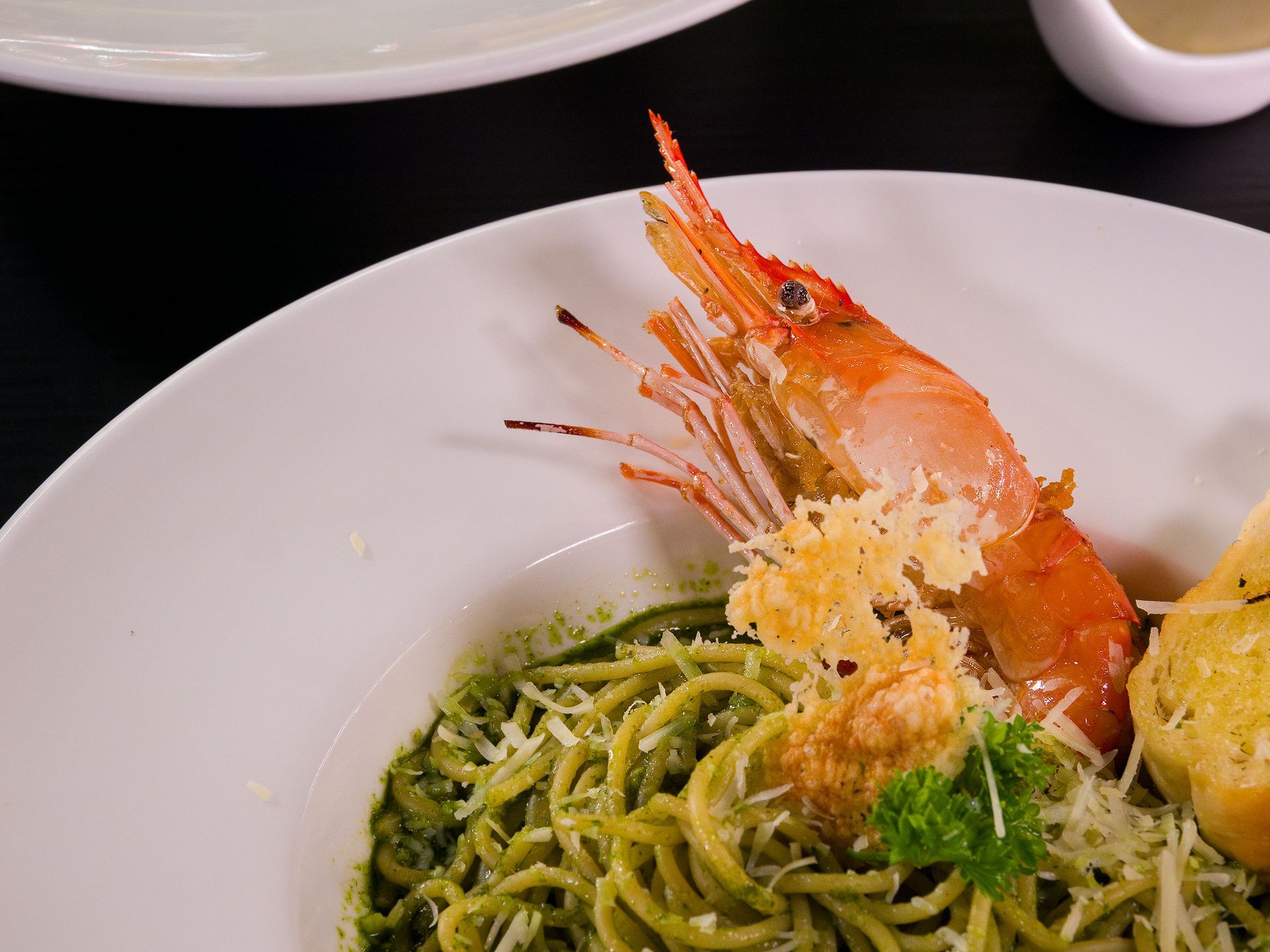 Pasta dish with pesto, shrimp, and garlic bread on a white plate.