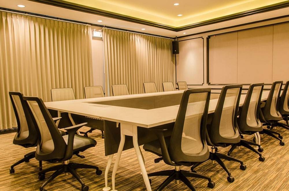 会议室里有一张长桌、黑色椅子、米色窗帘和暖色调的灯光。