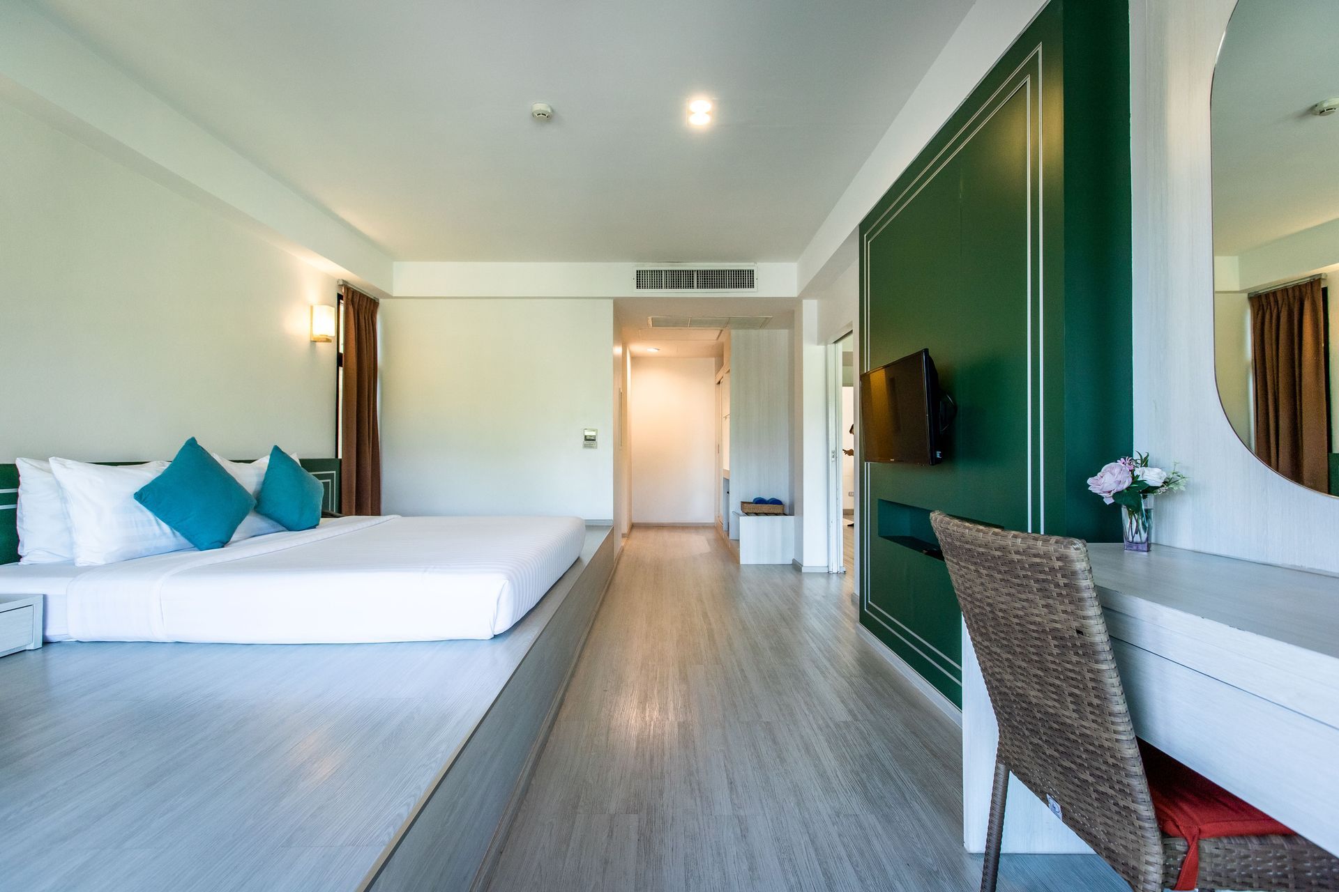 酒店房间内有白色床、绿松石色枕头、绿色装饰墙、书桌和大镜子。