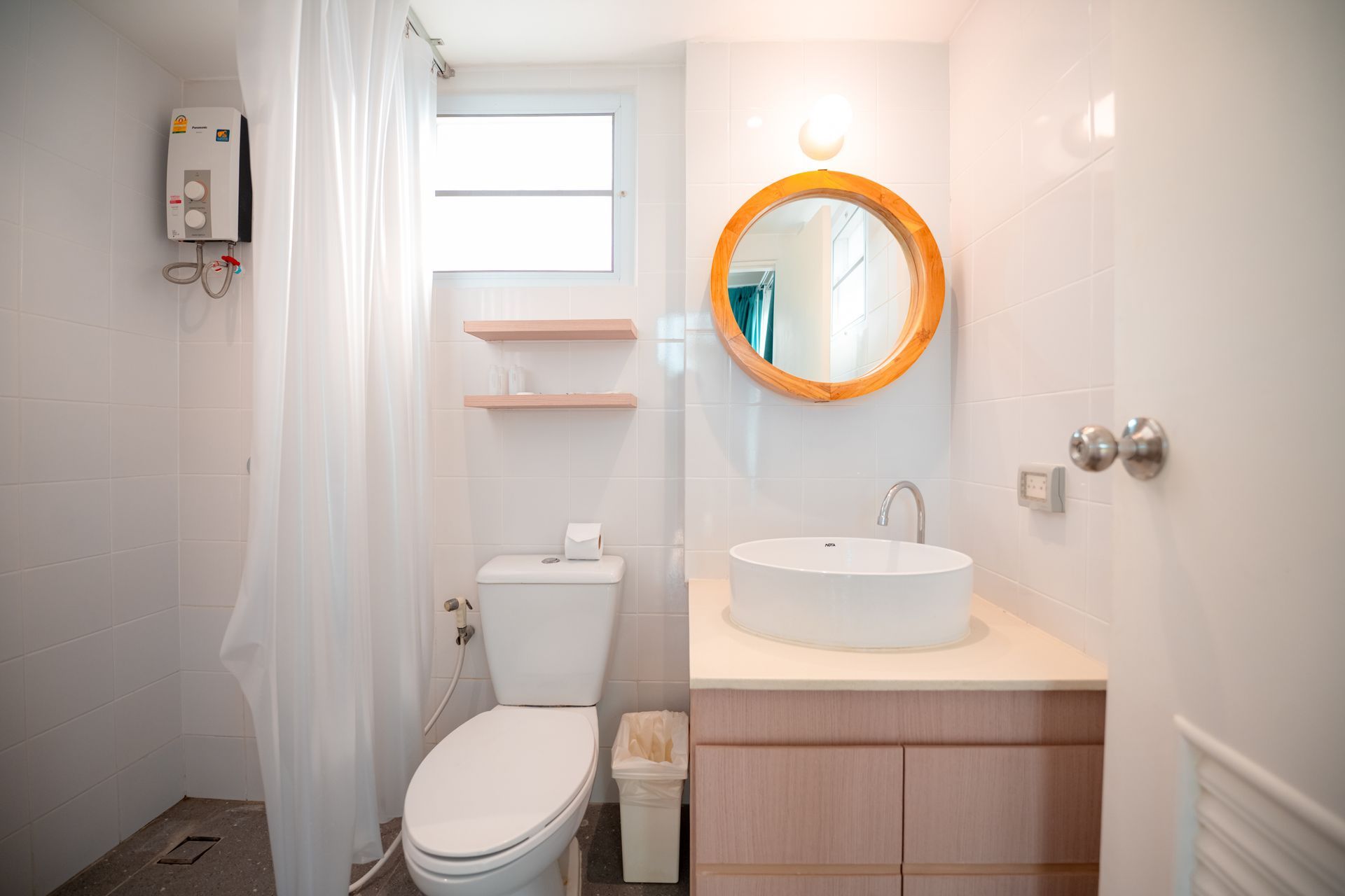 明亮的浴室，墙壁洁白，配有马桶、洗手池和木框圆形镜子。