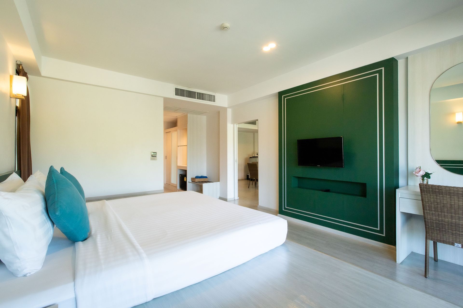 Hotel room with king-size bed, teal pillows, a green accent wall with TV, and a vanity.