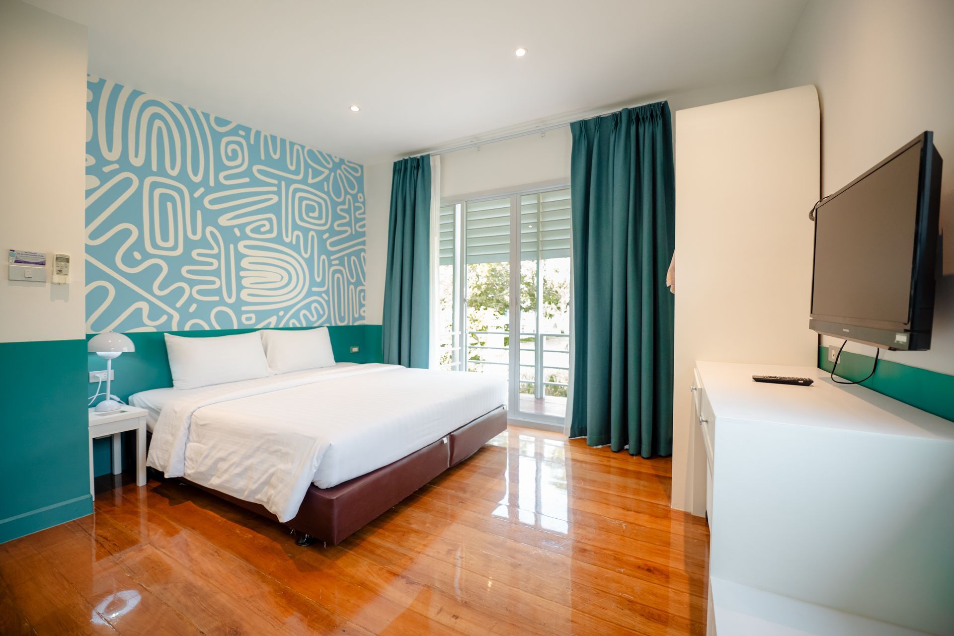 卧室里有一张大床、一面有图案的墙壁、蓝绿色的窗帘，以及放在白色梳妆台上的电视。