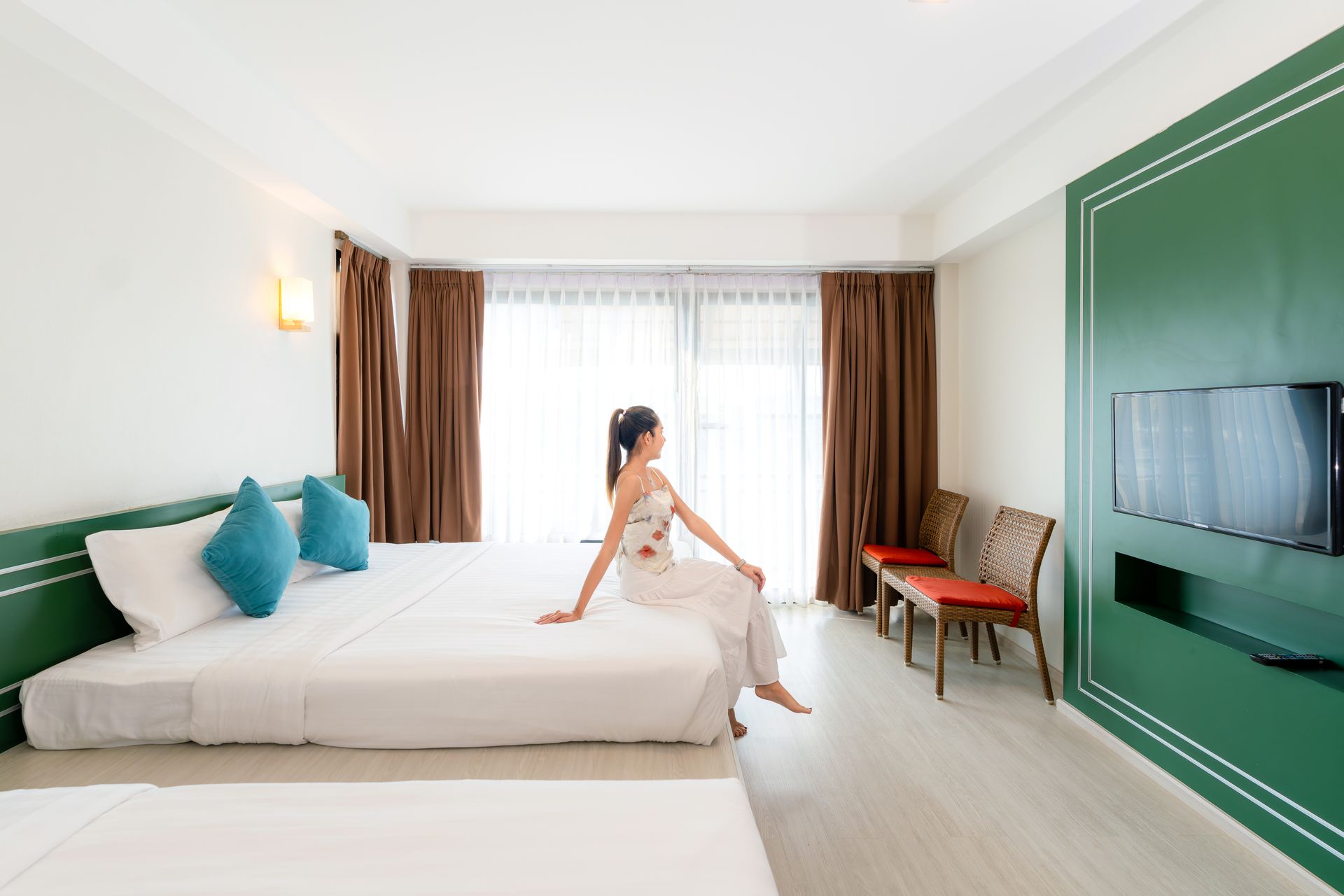 一位女士坐在酒店床上，望着窗外；房间明亮现代。