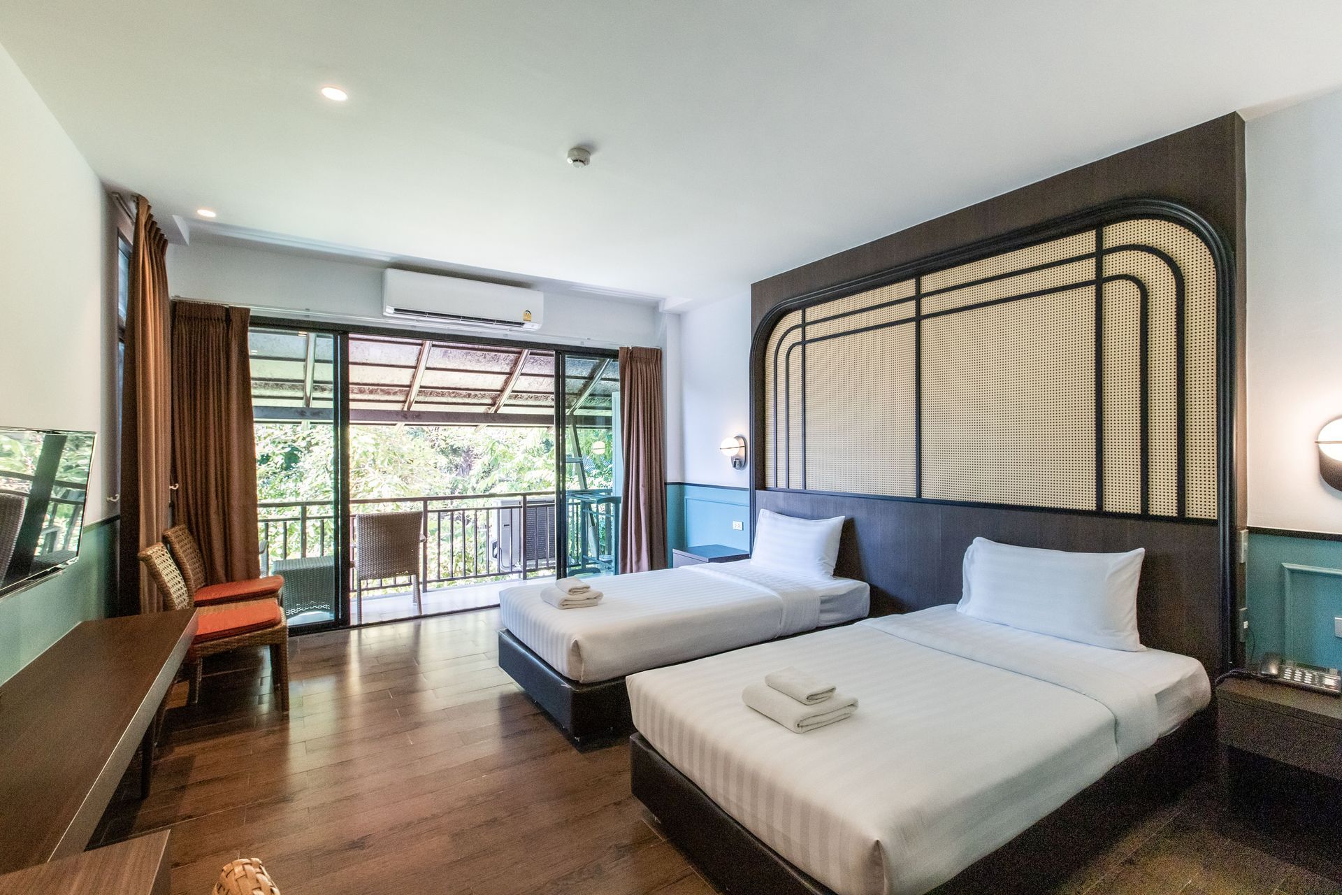 Hotel room with two beds, balcony access, wooden floors, and a dark accent wall.