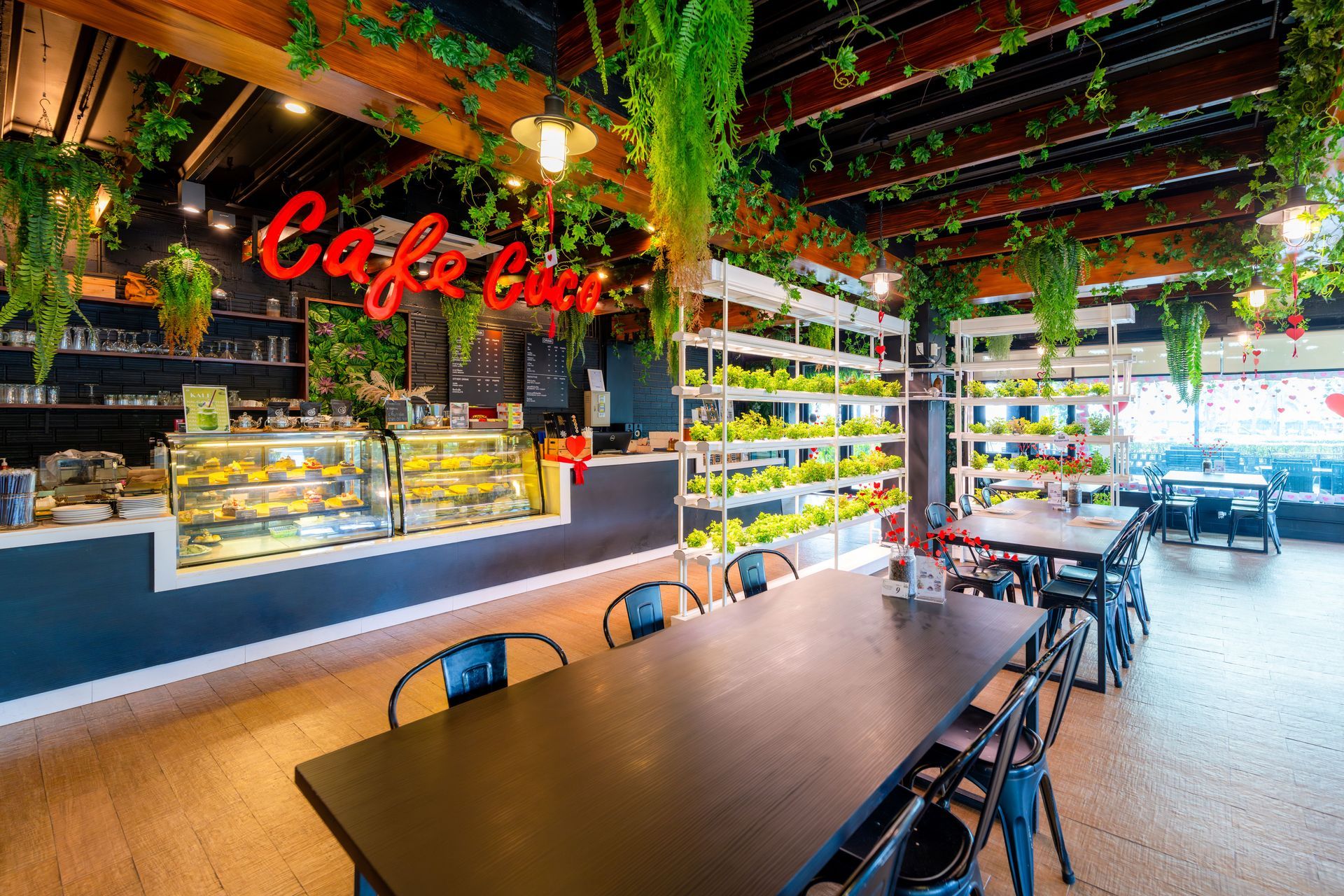 咖啡馆内部，摆放着黑色桌子、黑色椅子、糕点展示柜和悬挂的绿植。