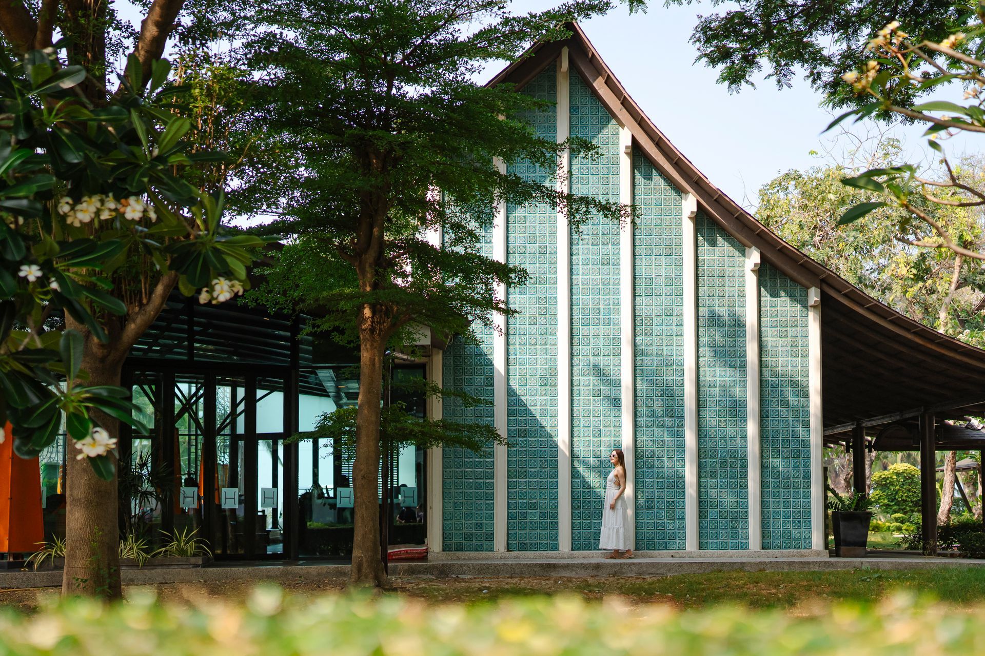 A person stands near a building with glass block walls and a pitched roof, surrounded by trees.