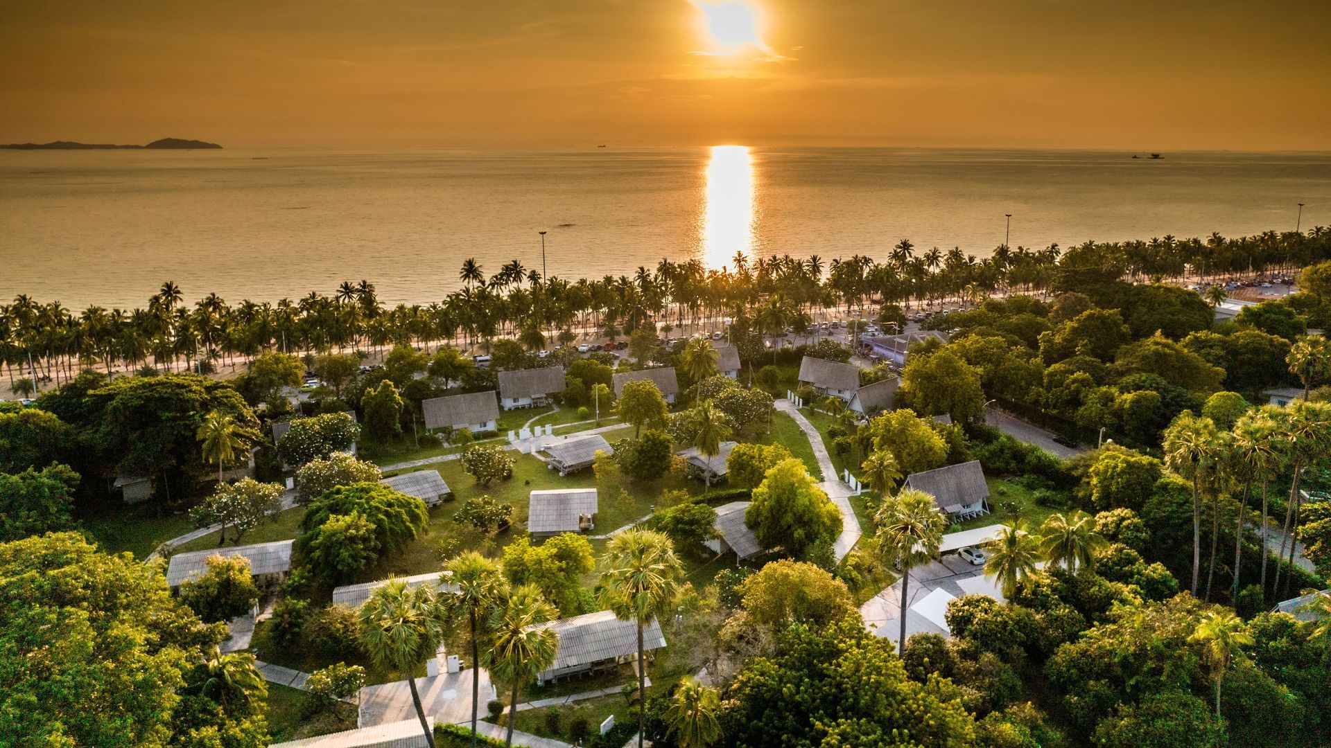 夕阳西下，映照着海滨度假村，别墅掩映在郁郁葱葱的树木之中；远处是蔚蓝的大海。