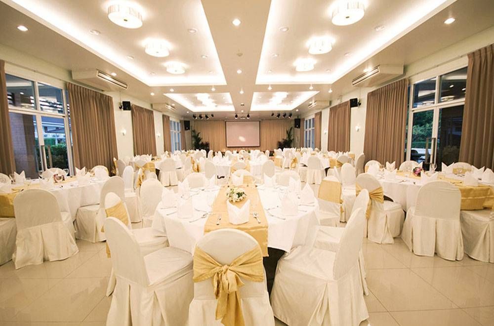 宴会厅内摆放着圆桌，布置成正式宴会的风格。桌布为白色，椅套为金色。