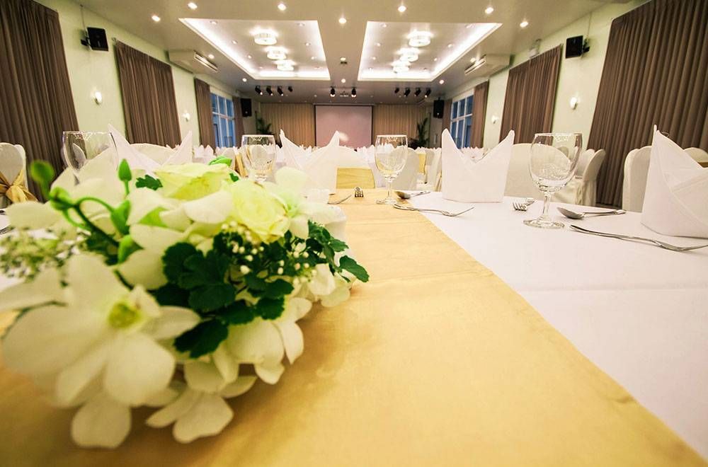 正式餐厅布置完毕，准备举办活动；金色桌布上摆放着花卉中心装饰品，铺着白色桌布，背景是舞台。