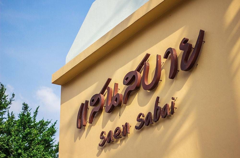 在棕褐色的建筑物上，蓝天背景下，用泰文写着“suen sabai”。