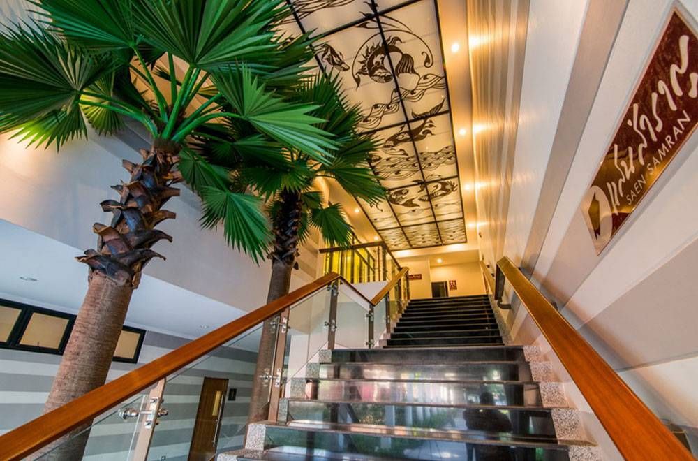 楼梯两侧有棕榈树、玻璃栏杆和装饰性天花板，通往一个昏暗的区域。