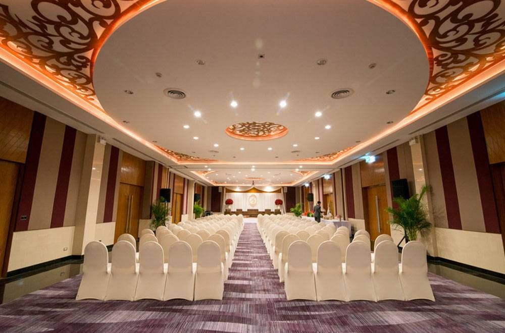 An empty banquet hall with rows of white chairs, ornate ceiling, and stage setup.