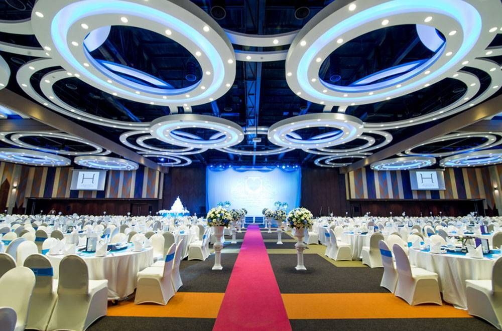 Large event hall with rows of tables, red carpet, and circular blue ceiling lights.