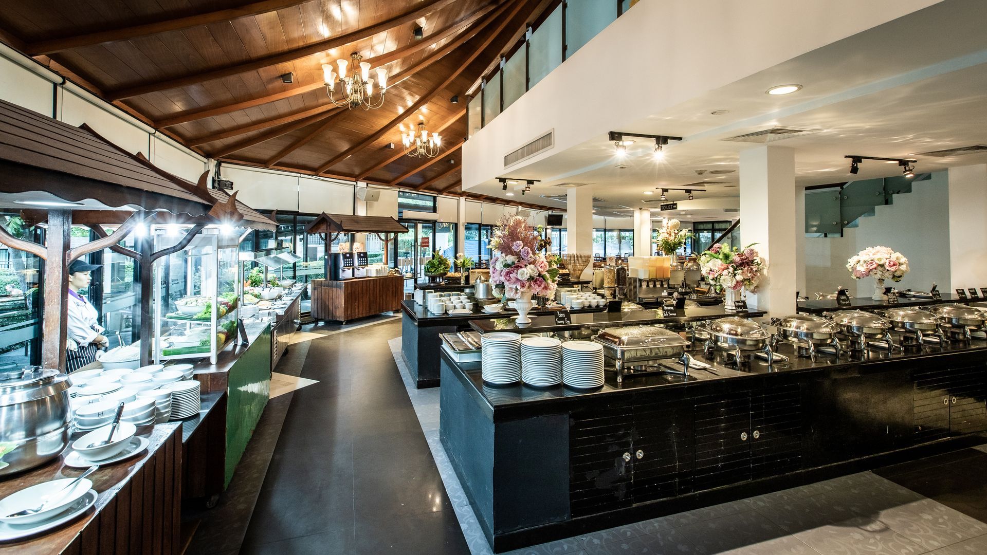 Buffet with food stations and dining tables in a brightly lit restaurant.