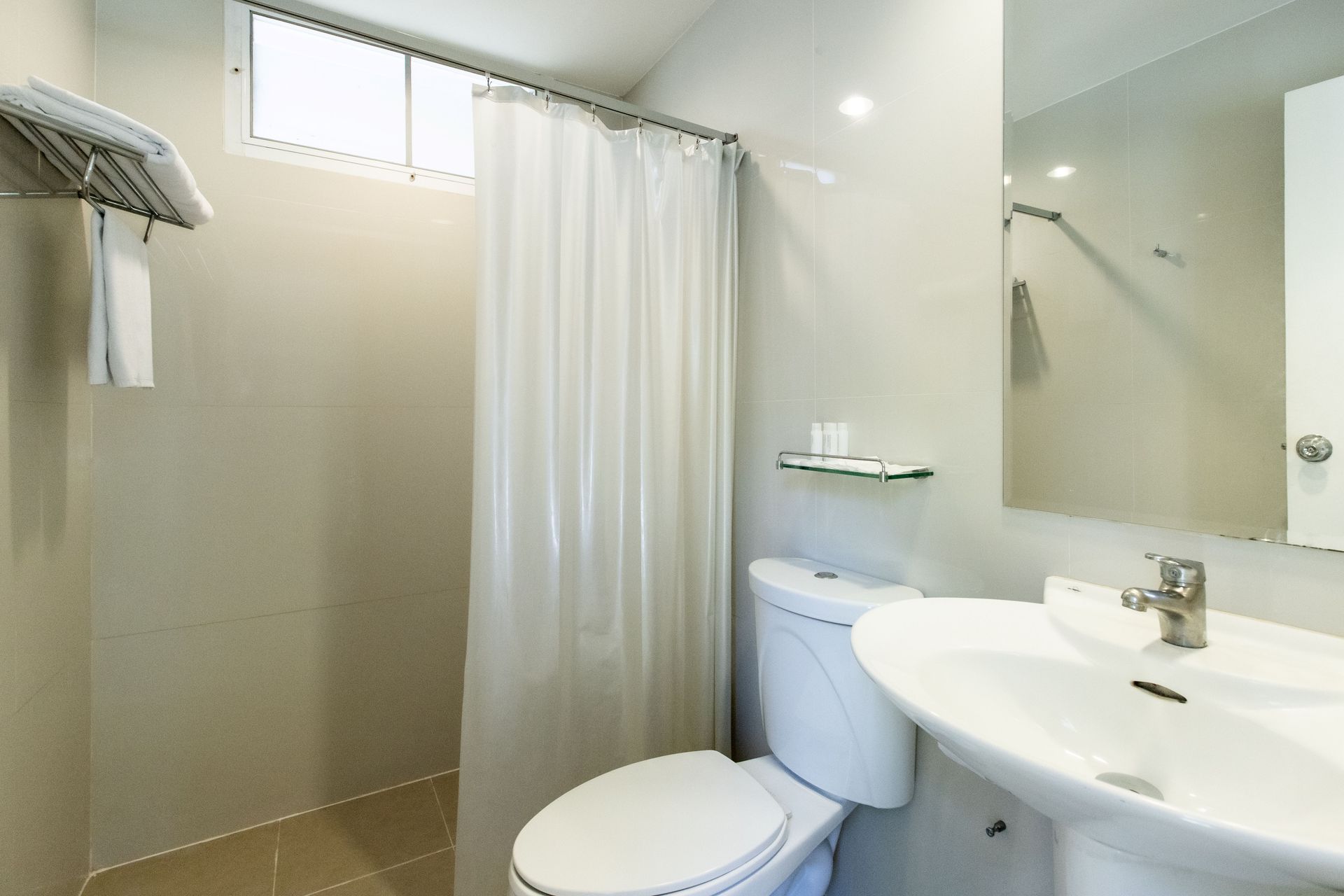 浴室配有白色洗手池、马桶、浴帘、毛巾和窗户。