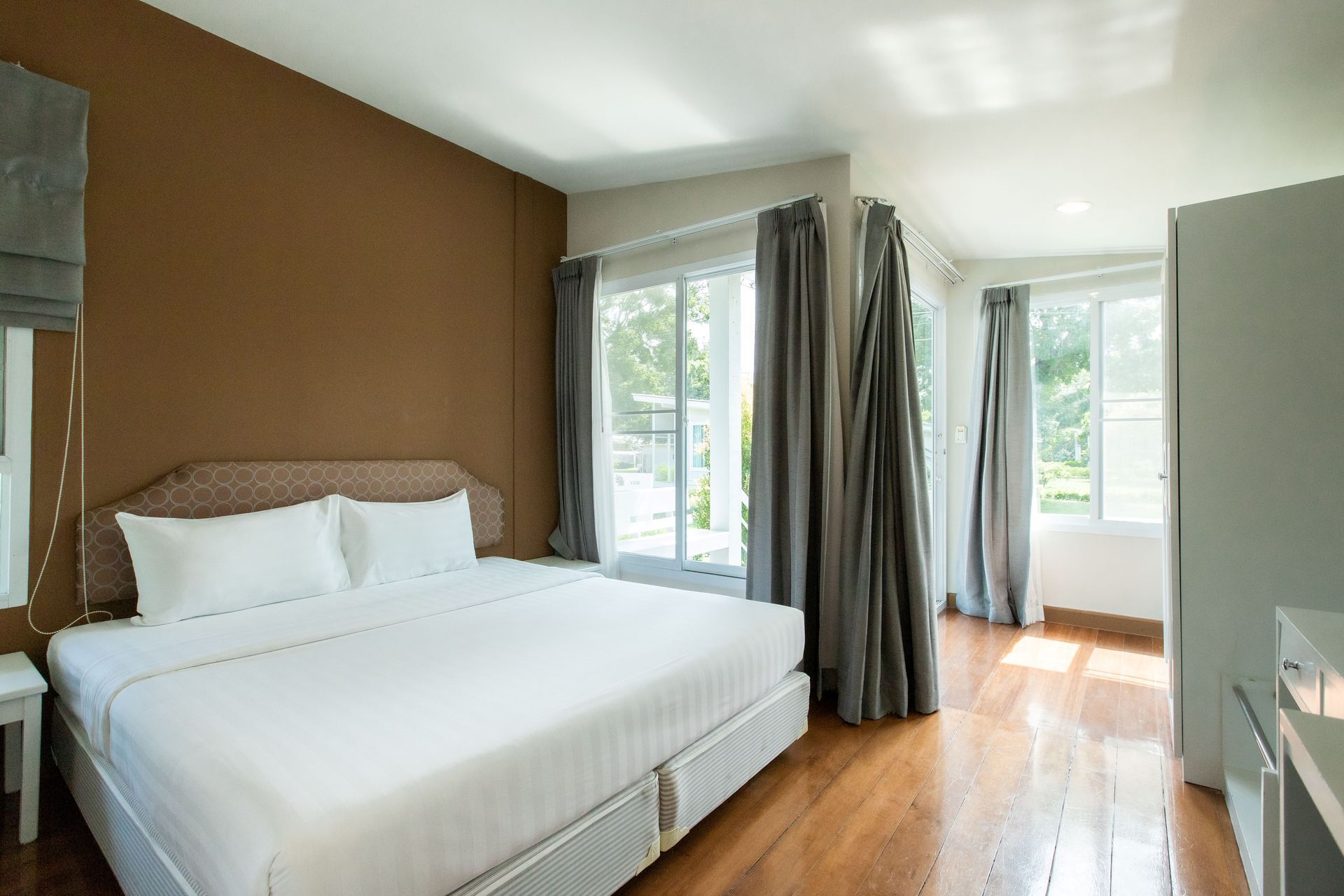 Bedroom with a bed, two windows with curtains, and a brown accent wall.