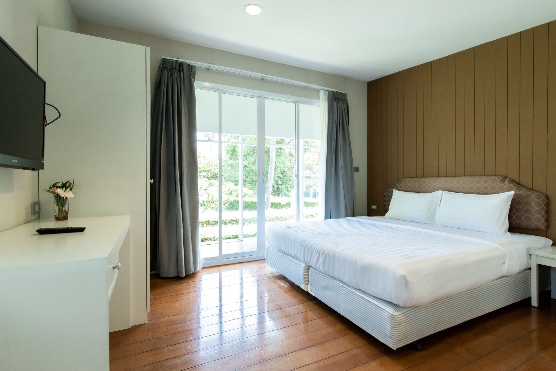 卧室配有白色床品、玻璃门、木板墙和电视。