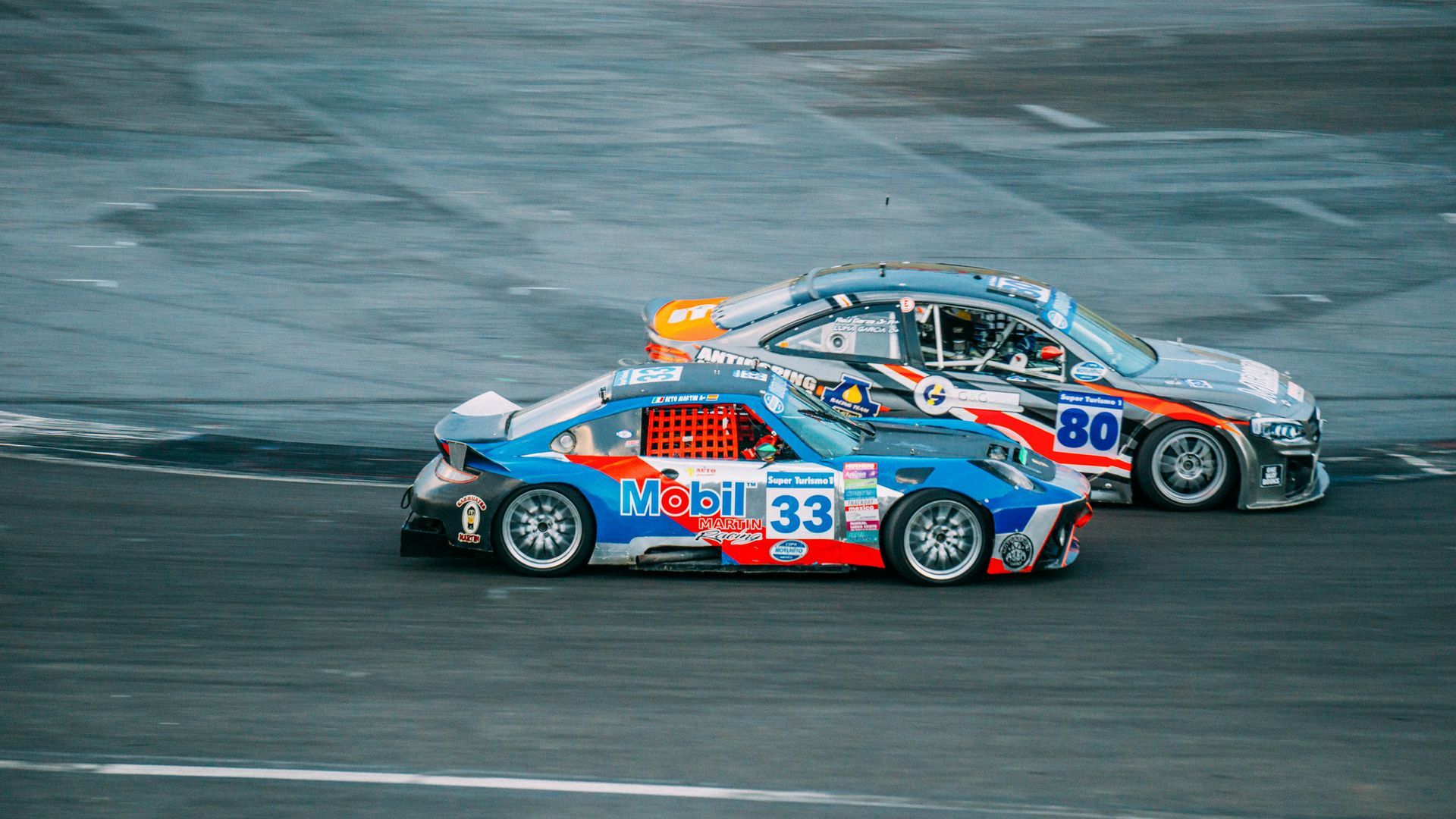 Two race cars, blue and silver, racing on a track.