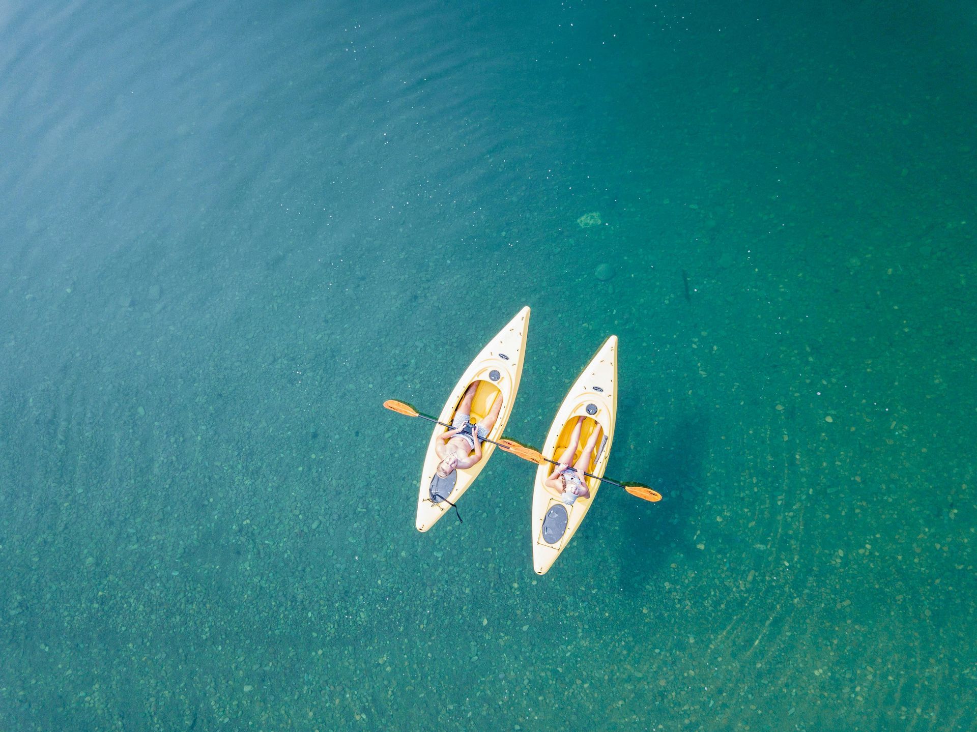 Two kayaks on teal water, seen from above. Paddles extend from the kayaks.