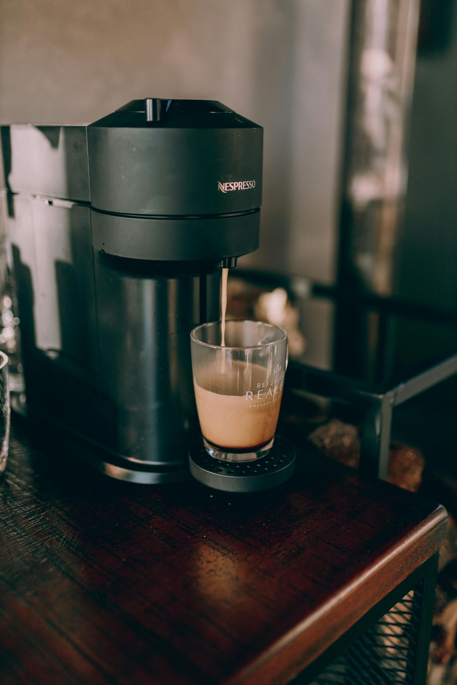 Black coffee maker dispensing coffee into a glass on a dark wooden table.