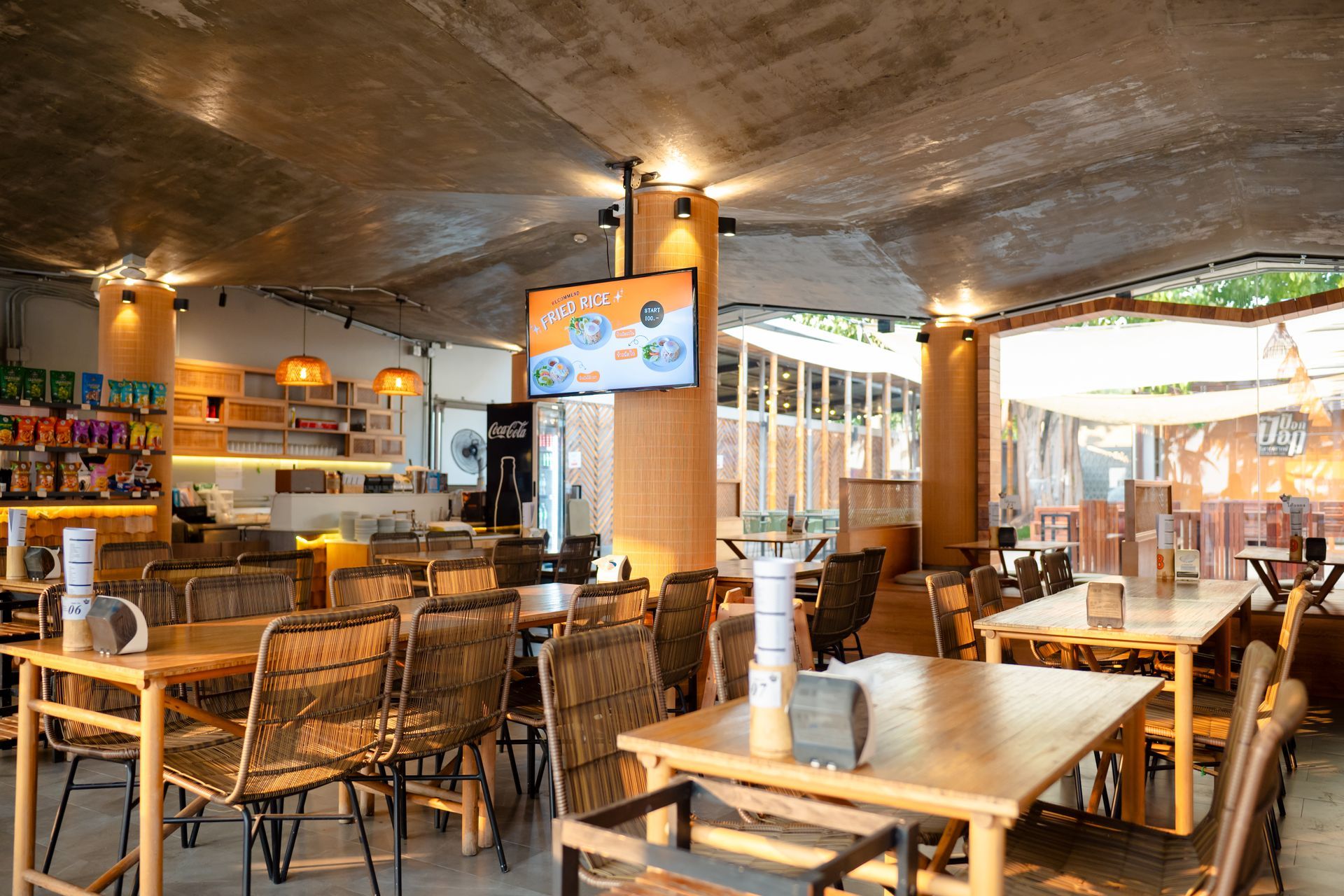 Restaurant interior with wooden tables, woven chairs, and a TV screen.