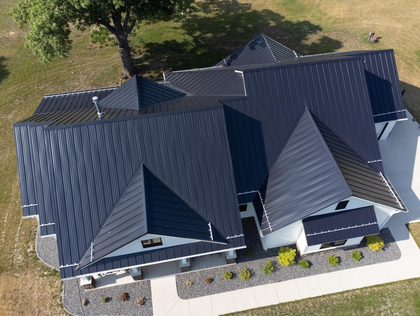 Aerial view of a modern house with a dark geometric patterned roof and white siding.