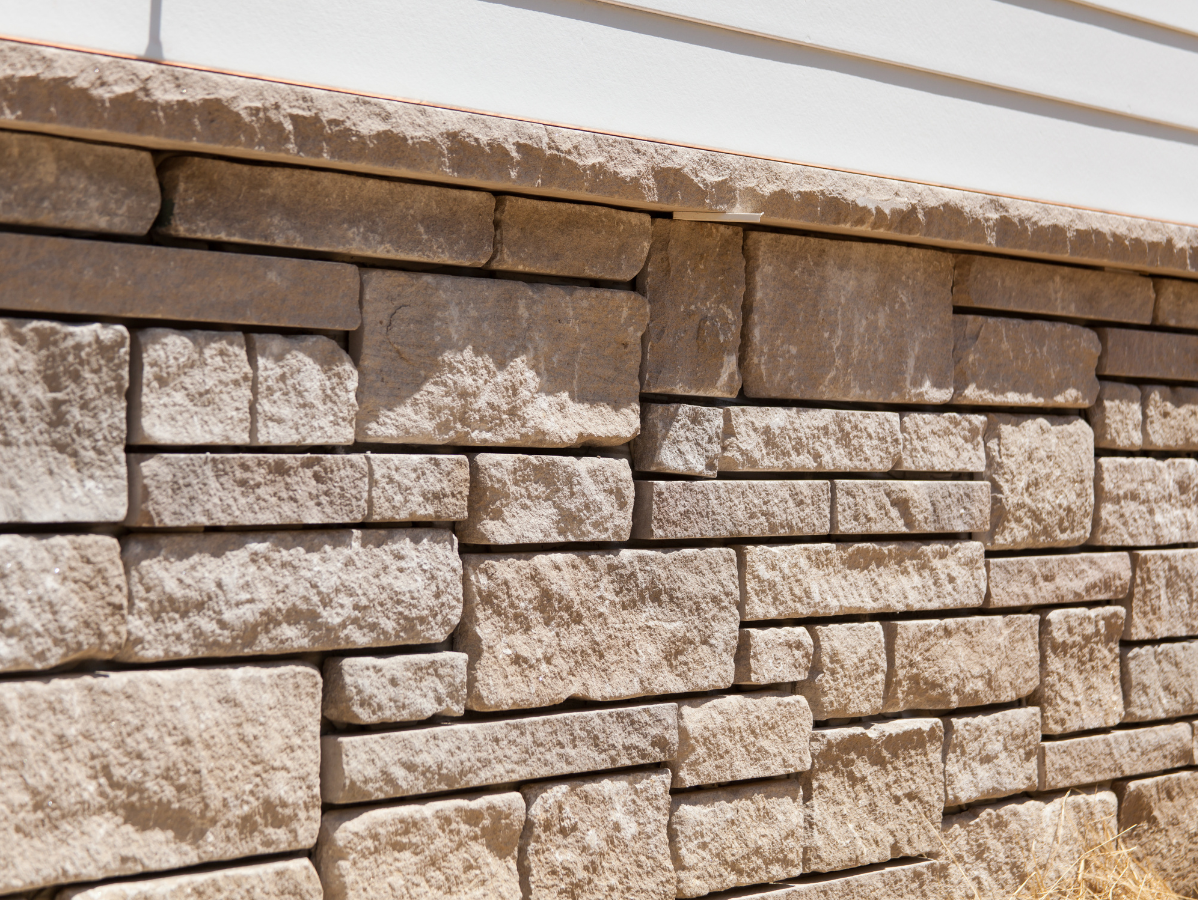 Stone block wall, tan color, beneath white siding.