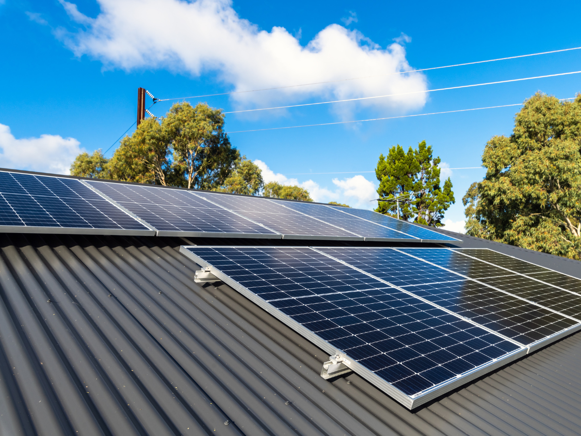 Solar panels installed on a black roof against a blue sky with clouds and trees.