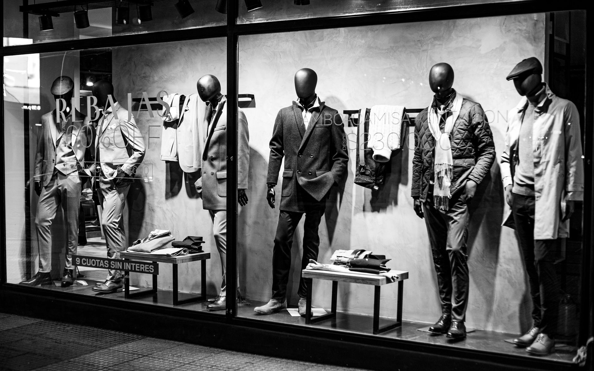Men's clothing store window display. Mannequins in suits, jackets, and accessories. Black and white.