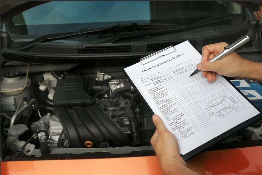 A Person Is Writing On A Clipboard In Front Of A Car Engine — Passfield Automotive and Electrical In Cessnock, NSW