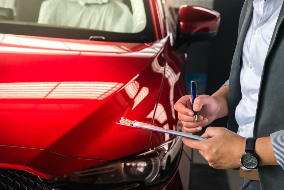 A Man Is Writing On A Clipboard In Front Of A Red Car — Passfield Automotive and Electrical In Cessnock, NSW
