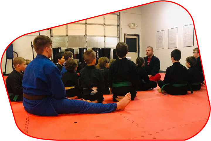 A group of kids are sitting on a mat in a gym