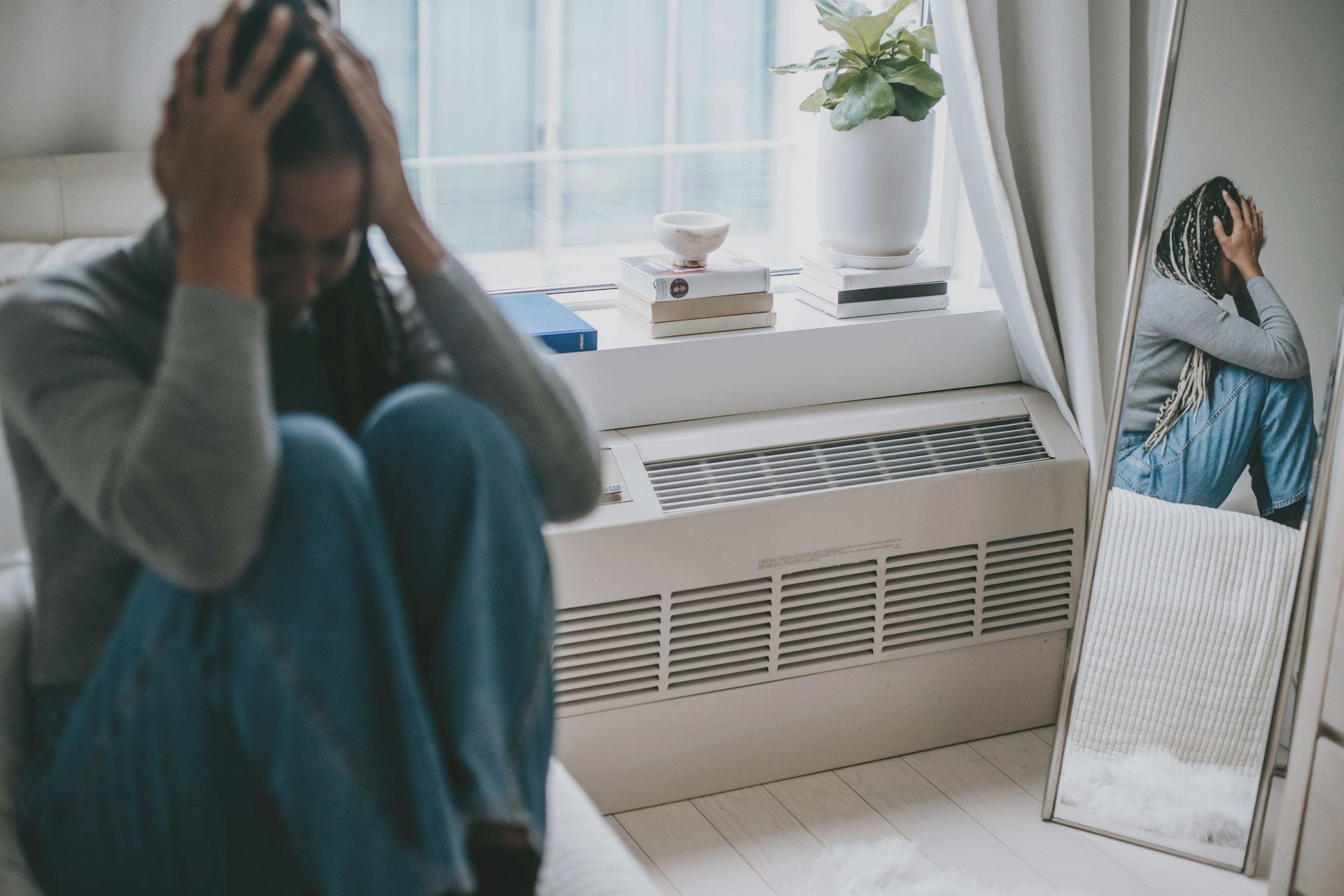 Person sitting on the floor with head in hands, reflecting stress and overwhelm, seen next to mirror