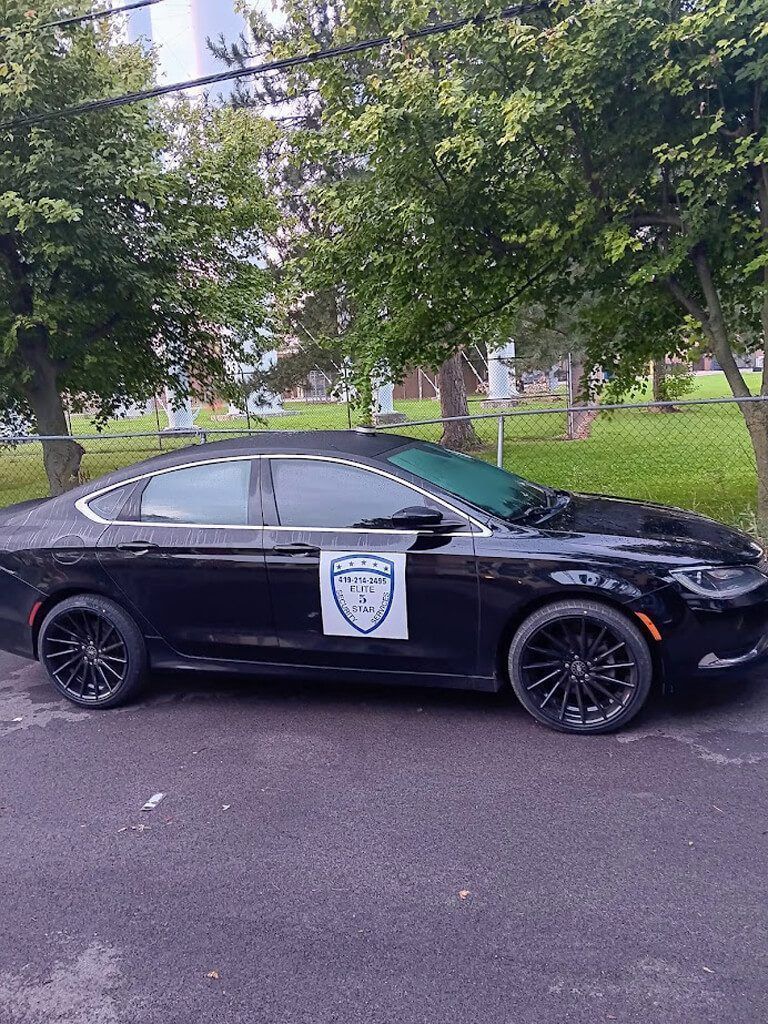 Black sedan with tinted windows parked on a street. It has a logo on the door and black rims.