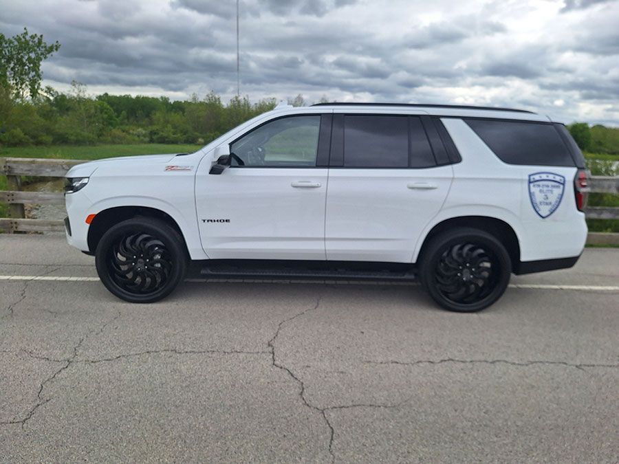 White SUV with black wheels, parked on a road, likely a police vehicle.