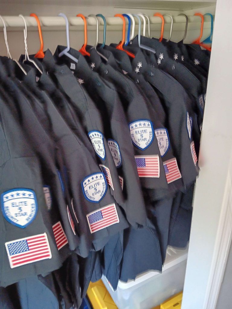 Navy blue shirts hanging in a closet, each with an American flag and 