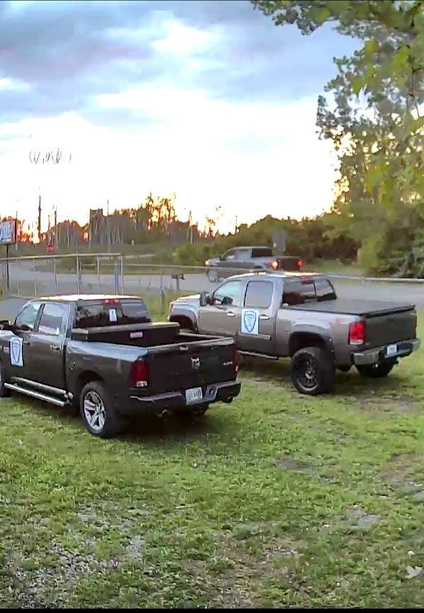 Three pickup trucks parked on grass near a fence. Dark, cloudy sky.