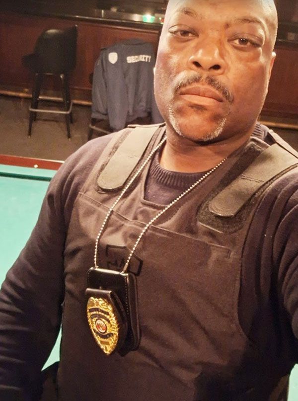 Security guard with a badge and vest, stern expression. Inside a bar, pool table in view.