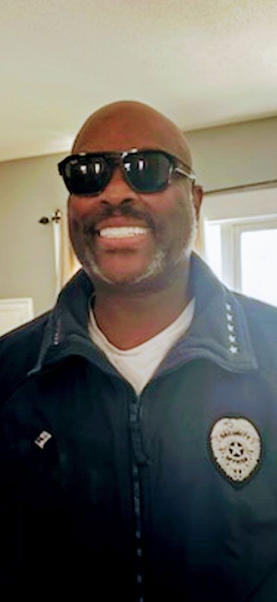 Man with sunglasses smiling in a uniform with a badge.