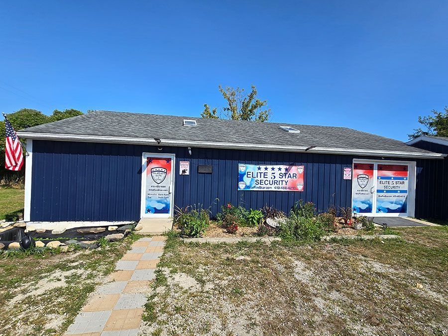 Blue building with security signage, American flag, and a walkway under a blue sky.