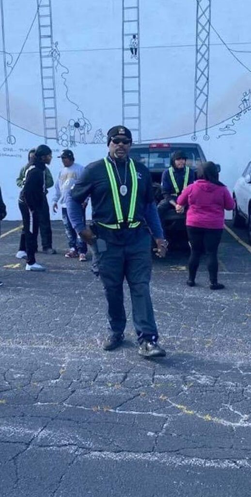 Security guard in reflective vest directs people in a parking lot.