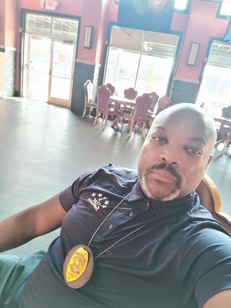 Man in blue shirt with badge, sitting, in restaurant.