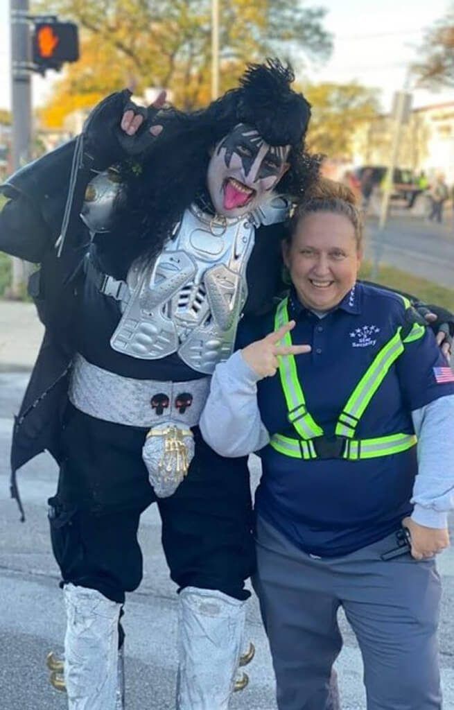 Person in KISS makeup and costume poses with a woman in a work uniform; they are smiling.