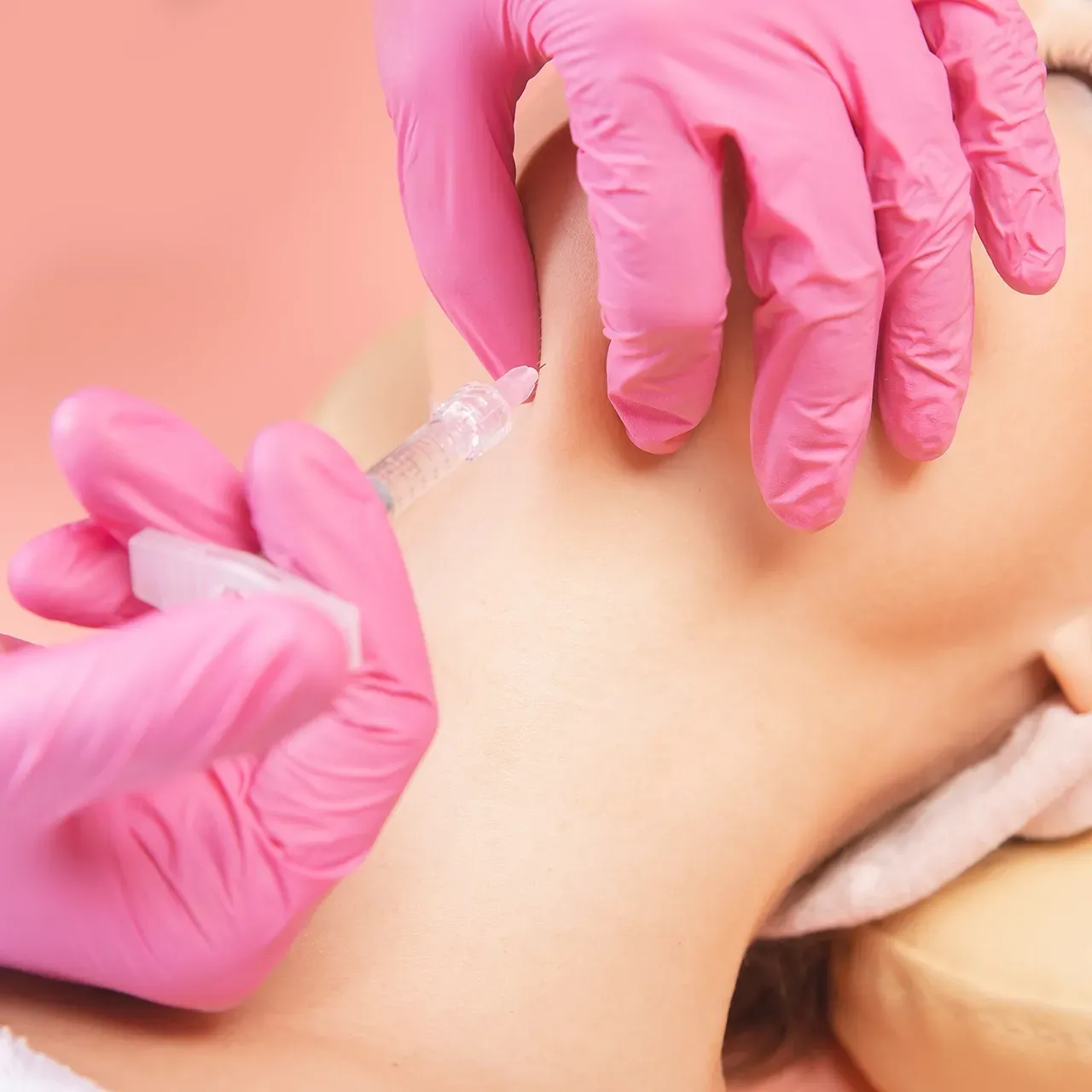 A woman wearing pink gloves is getting a facial treatment.