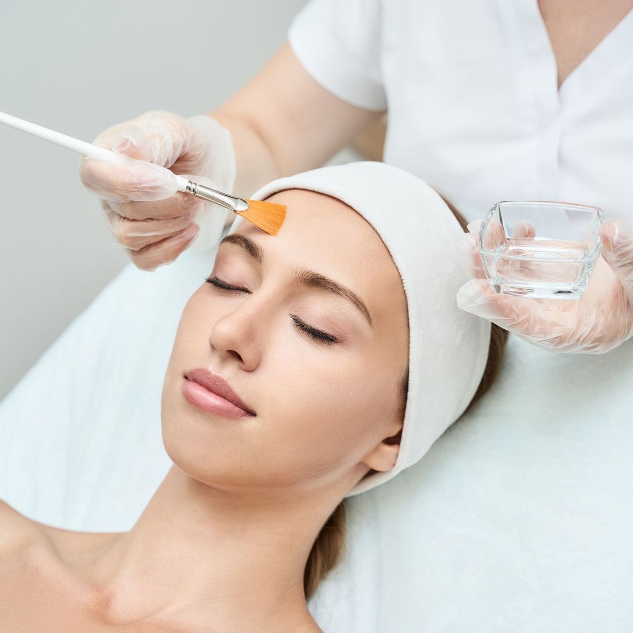 A woman is getting a facial treatment with a brush on her forehead.