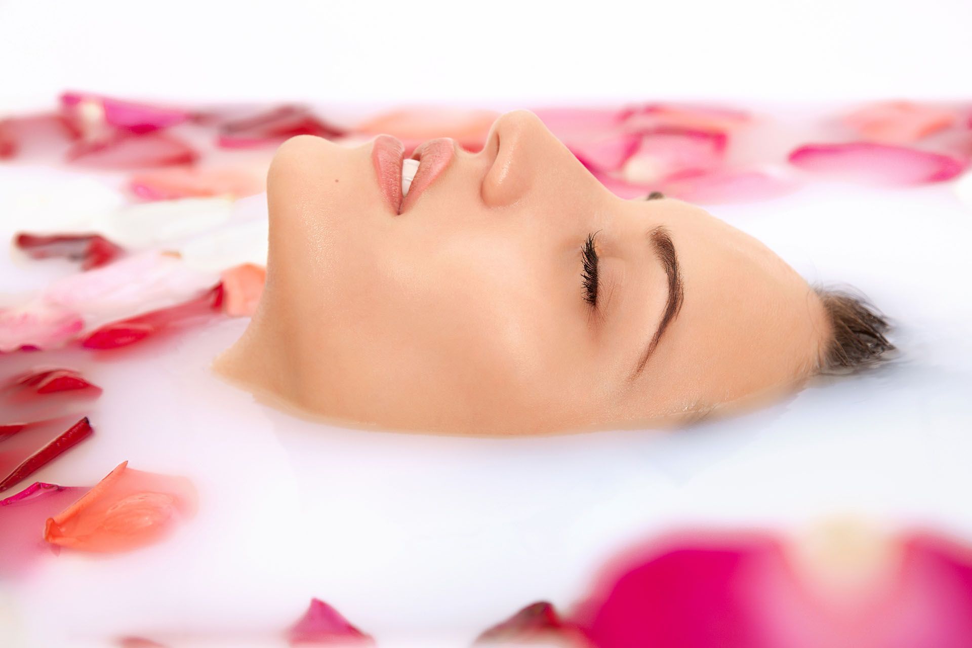 A woman is laying in a bathtub filled with milk and rose petals.